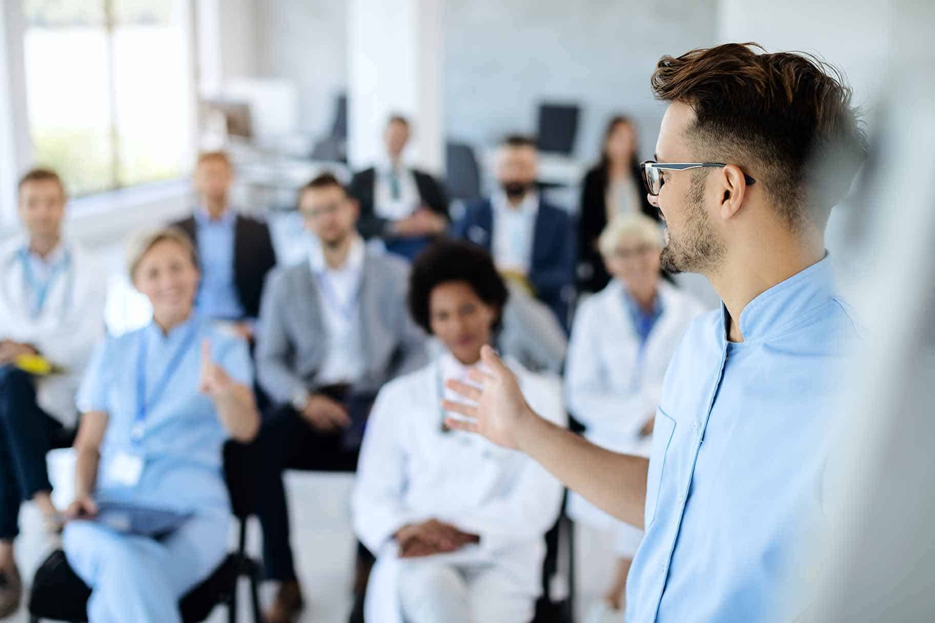 MOL-HA.flip a healthcare administrator standing and leading a presentation to a group of seated peers