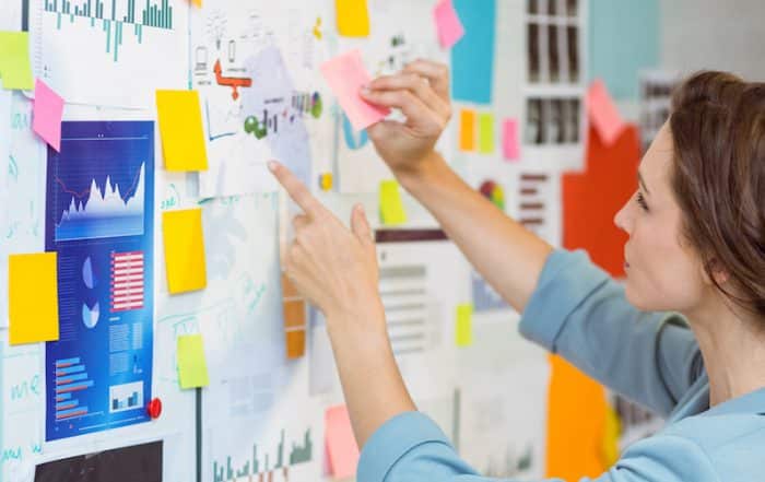 a woman standing and observing a wall of charts, graphs and sticky notes