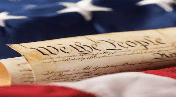 the U.S. Constitution with an American flag in the background